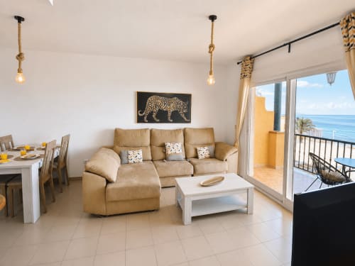 Salón de apartamento frente al mar con vistas al océano, sofá color arena, mesa de café blanca, zona de comedor y balcón con vista al océano en Cuevas