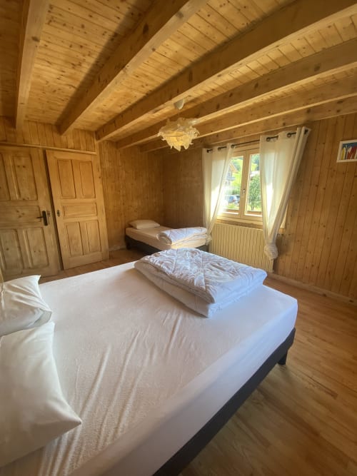 Spacious wooden chalet bedroom with double bed, single bed, beamed ceiling, and mountain views at La Ferme des Georgières,