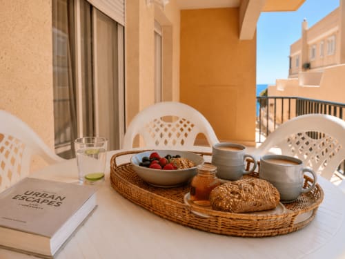 Desayuno servido en la terraza de Apartamentos El Calón Playa con vistas al mar, pastelería fresca, frutero y tazas de café