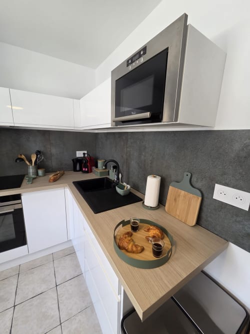 Cuisine moderne à la Résidence Cosy à Saint-Méen-le-Grand avec armoires blanches, crédence sombre, comptoirs en bois et électroménagers inox