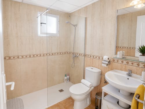 Modern bathroom in Apartamentos El Calón Playa with beige tile, glass shower, white toilet, sink and mirror in Cuevas del