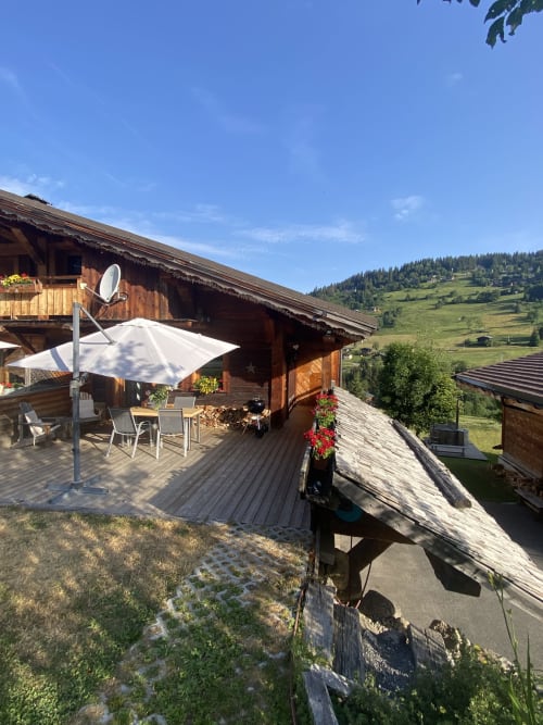 Chalet alpin en bois avec terrasse, parasol blanc et vue sur les montagnes à Notre-Dame-de-Bellecombe