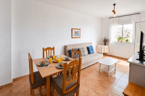 Bright living-dining area in Apartamentos El Calón Playa with wooden furniture, sofa, and sea views through windows