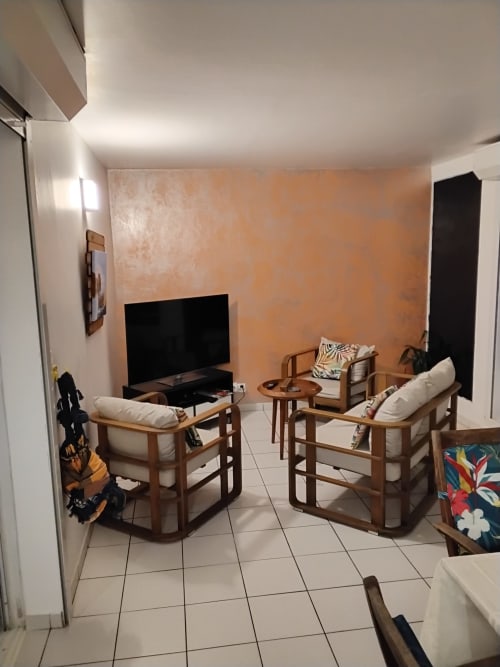 Salon moderne de l'hôtel Kay Betty en Martinique avec mobilier en bois, TV écran plat et mur d'accent pêche