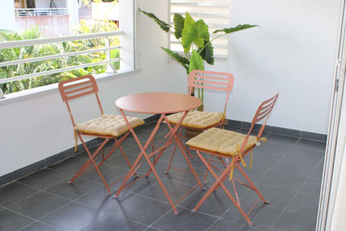 Ensemble de salle à manger en corail avec chaises rembourrées et plante en pot sur balcon d'appartement moderne avec vue sur jardin