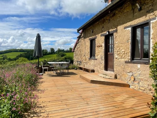 Terrasse en pierre du Château de Vaux Mordan avec terrasse en bois, vue sur le jardin et paysage vallonné français
