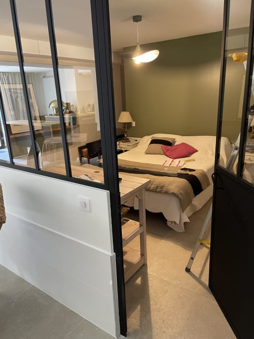 Chambre moderne aux Pratges Figeac avec paroi vitrée, lit à coussin rouge, mur d'accent vert et luminaires suspendus