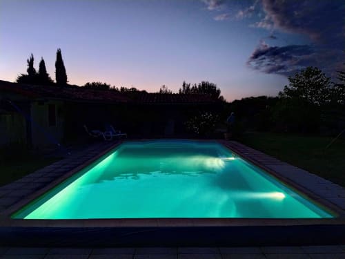 Glowing turquoise swimming pool at twilight, Les Gites de Campardon in Montés, France, surrounded by gardens and loungers