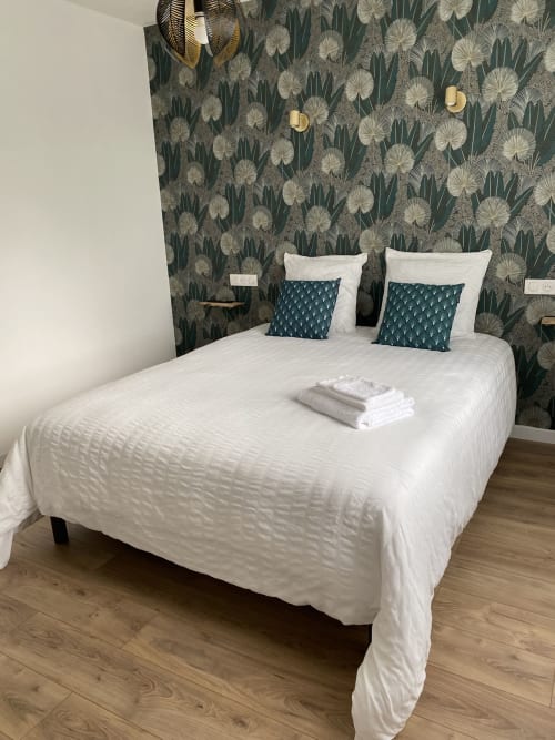 Chambre élégante de l'appartement La Maison Blanche avec linge blanc, oreillers turquoise, papier peint à motifs et parquet