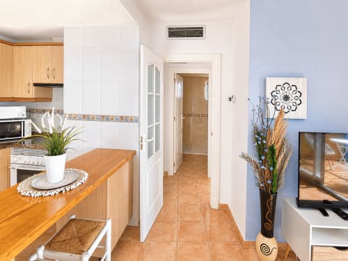 Modern kitchen-living area in Apartamentos El Calón Playa with wooden cabinets, white walls, tiled flooring, and decorative