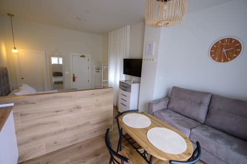 Interior de estudio de hotel moderno con recepción, sofá gris, mesa de comedor de madera, televisor y cocina en Salobreña
