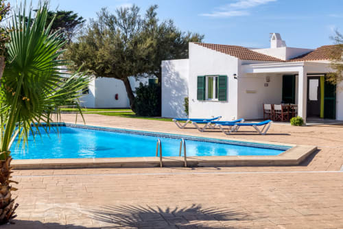 Villa Las Golondrinas con piscina de aguas cristalinas, edificio encalado, tumbonas y palmeras en Cap d'Artrutx