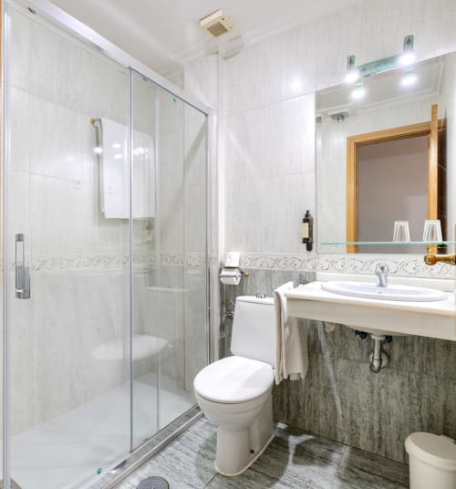 Baño moderno en Hostal El Molino con ducha de cristal, lavabo blanco, inodoro y espejo con marco de madera
