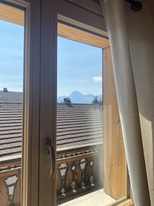 Open wooden door overlooking mountain view, rooftop terraces, and Alpine peaks from La Ferme des Georgières apartment