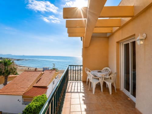 Beachfront terrace at Apartamentos El Calón Playa with sea view, wooden pergola, white furniture, and Mediterranean coastline