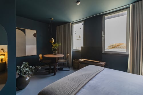 Quarto moderno de hotel no Porto com paredes azul-petróleo escuro, cama, mesa de refeições e janelas com vista para a cidade