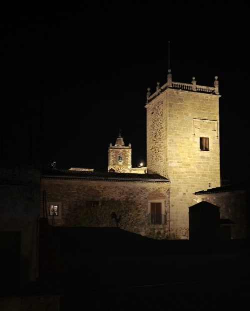 Torre de iglesia de piedra histórica iluminada de noche en Cáceres, España - vista del mirador medieval