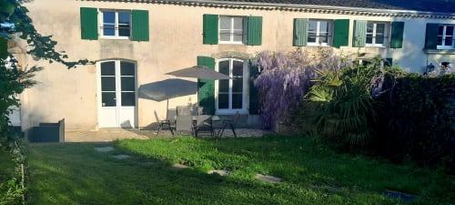 Garden view of Logis de Chenac cottage with terrace seating, wisteria, and palm plants in Chenac-Saint-Seurin-d'Uzet, France