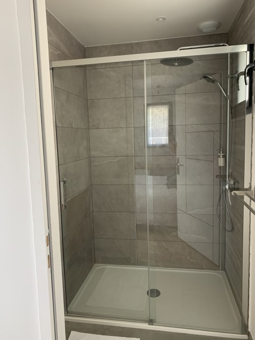Modern glass-enclosed shower with gray tile walls and rainfall showerhead in La Maison Blanche boutique hotel room,