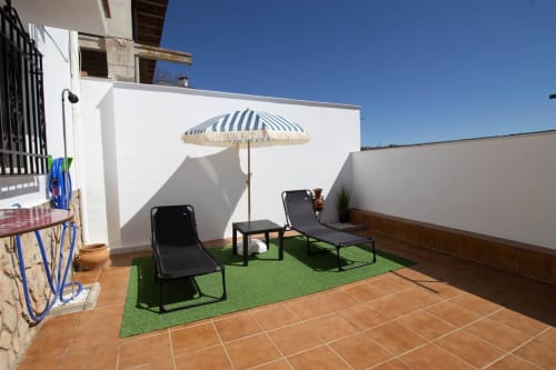 Soleada terraza en la azotea de La Casa de Tita Clota en Setenil de las Bodegas con tumbonas, sombrilla rayada y blanco