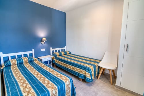 Dormitorio doble en Las Golondrinas con pared de acento azul, ropa de cama rayada y muebles blancos modernos en Cap d'Artrutx