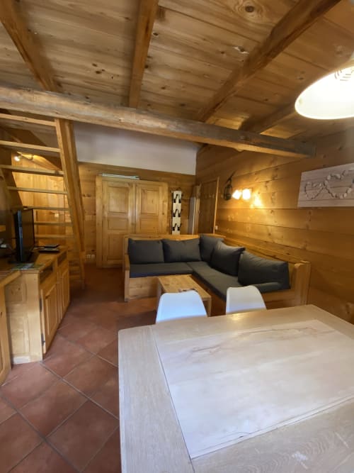 Séjour chaleureux en bois avec table à manger, canapé gris foncé et vue sur les montagnes à La Ferme des Georgières