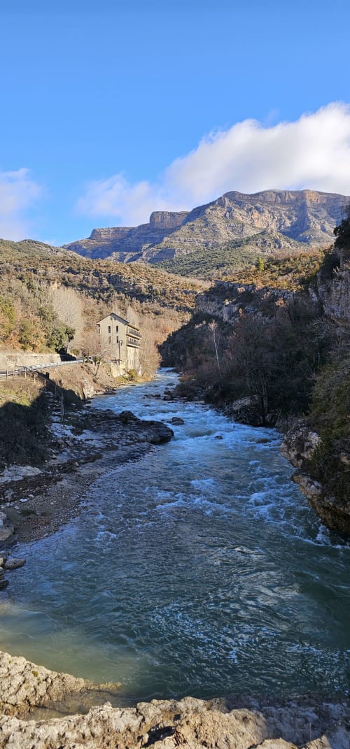Río de montaña y edificio de piedra en un valle del Prepirineo con picos dramáticos y cielo azul despejado