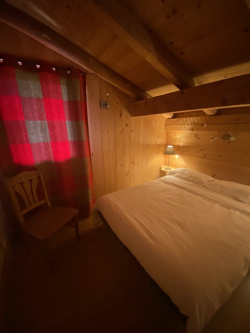 Chambre cosy en bois à La Ferme des Georgières avec lit queen-size, rideaux à carreaux rouges et éclairage chaleureux