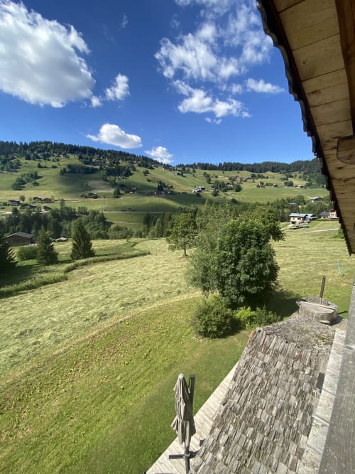 Vue panoramique de la vallée montagnarde depuis la terrasse de La Ferme des Georgières à Notre-Dame-de-Bellecombe, collines verdoyantes et