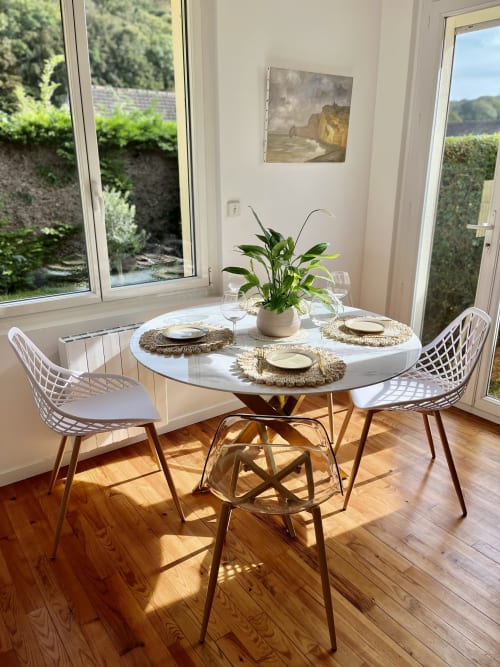 Salle à manger contemporaine avec table ronde blanche, sets de table tissés, plante en pot et vue sur le jardin au gîte ART DE VOYAGER