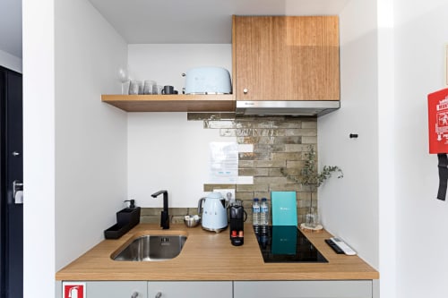 Pequena kitchenette em estúdio de hotel no Porto com bancadas de madeira, pia, fogão, cafeteira e paredes brancas