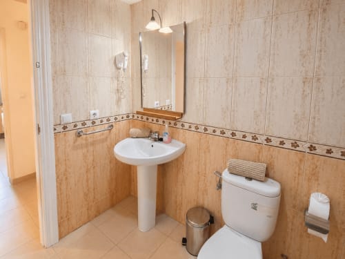 Baño accesible en Apartamentos El Calón Playa con lavamanos pedestal, inodoro, barra de apoyo y paredes alicatadas