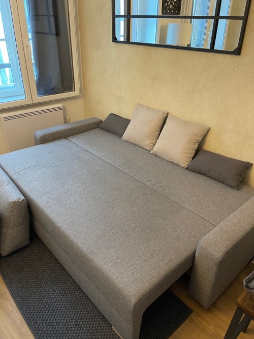Canapé-lit convertible gris dans l'appartement Le Charmant Paillot à Troyes, avec coussins beige et murs en papier peint jaune