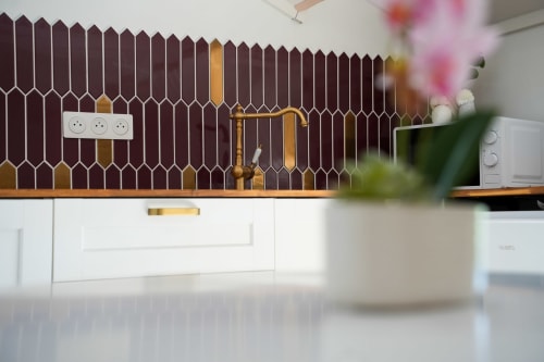 Cuisine moderne avec dosseret hexagonal bordeaux et or, armoires blanches, et fleurs en pot aux Séjours Ardennais