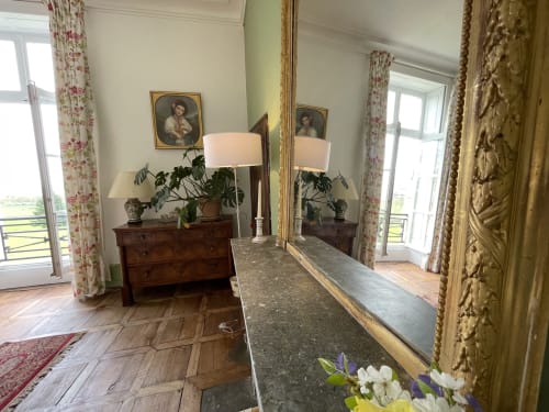 Chambre élégante du château de Vaux Morvan avec commode ancienne, miroir, lampes et vue sur le jardin