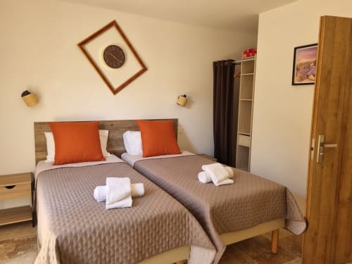 Twin beds with orange pillows in a bright bedroom at L'Orée du Ventoux, Crillon-le-Brave, with pool view and modern amenities