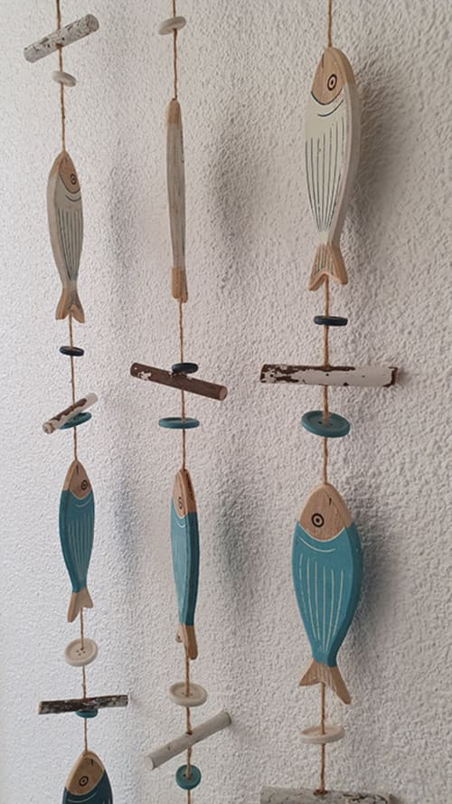 Handcrafted wooden fish mobile with turquoise and cream details hanging on white wall in Cap Coz apartment, La