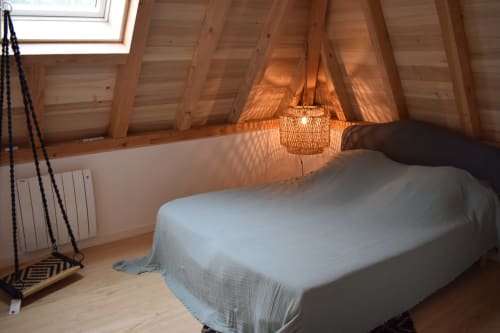 Chambre lumineuse sous les toits avec poutres apparentes, lit blanc, suspension en rotin et balançoire aux Pratges Figeac