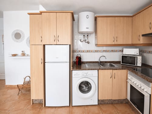 Compact kitchen with wooden cabinets, white appliances, and granite countertop in Apartamentos El Calón Playa, Cuevas del