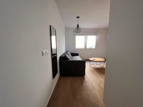 Sala de estar moderna en El HierroStay Apartments, La Restinga, con sofá negro, pisos de madera y vistas a la ciudad