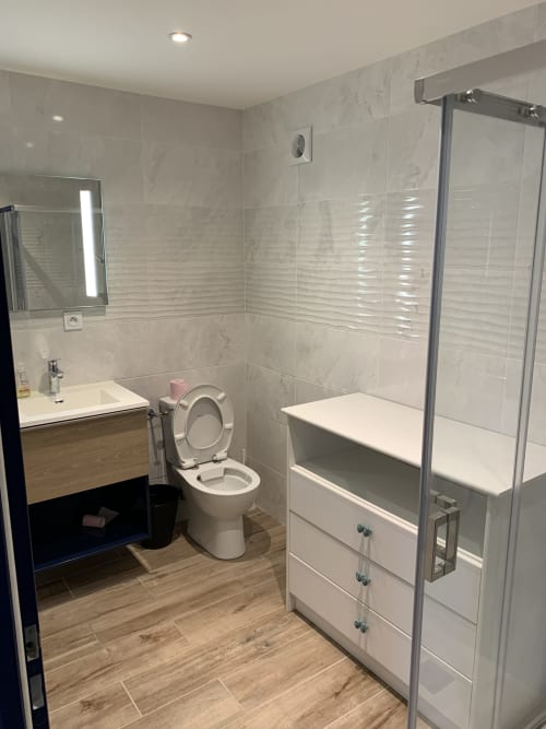 Salle de bains moderne du B&B Le Restaurant du Port à Saint Pierre de Boeuf avec carrelage marbre, lavabo, toilettes et douche vitrée