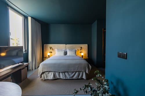 Quarto de estúdio moderno em hotel no Porto com paredes azul-petróleo, cama com iluminação amarela de destaque, TV de tela plana e vistas para a cidade