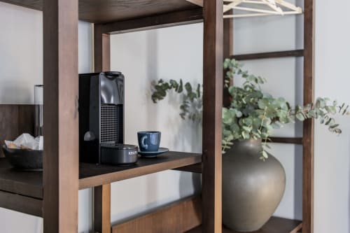 Kitchenette compacta com máquina Nespresso, xícara de café, plantas e prateleiras de madeira no hotel Benefit Collection Porto