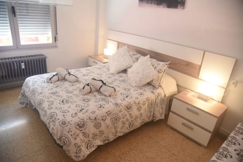 Bedroom in Benavente apartment with queen bed, patterned bedding, white pillows, wooden headboard, nightstands, and window