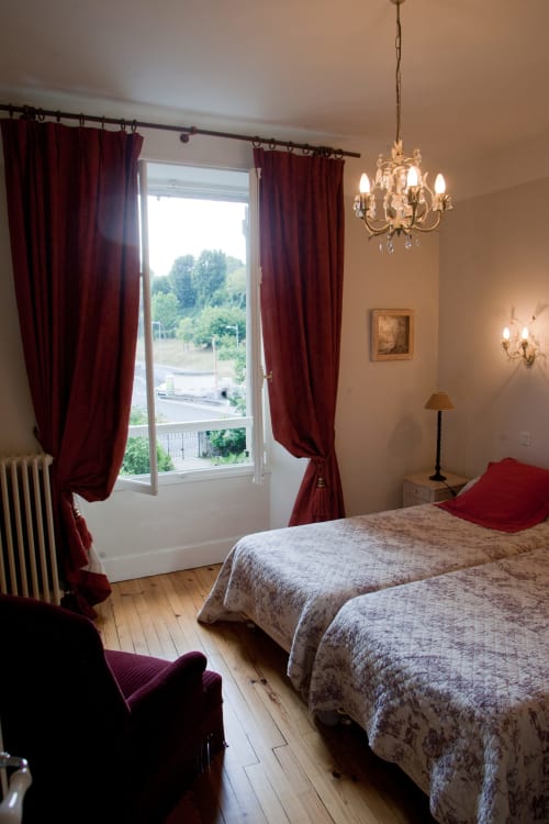 Élégante chambre double aux Chambres d'hôtes Les Pratges à Figeac avec rideaux bordeaux, lustre et vue sur le jardin
