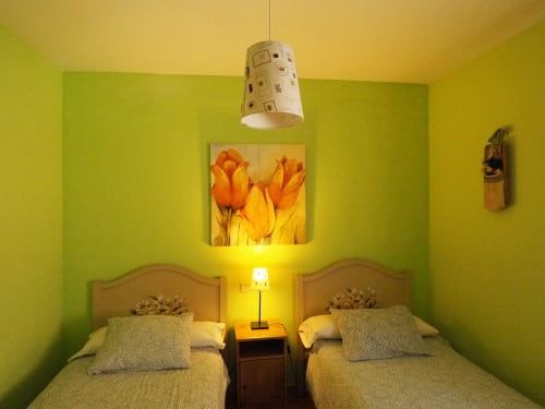 Dormitorio luminoso en Rural Senda del Duratón con camas gemelas, paredes amarillas y cuadros con tulipanes en Sebúlcor