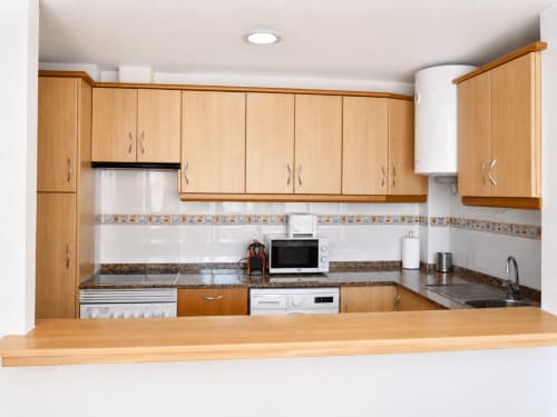 Modern kitchen in Apartamentos El Calón Playa with wooden cabinets, granite counters, and equipped appliances including
