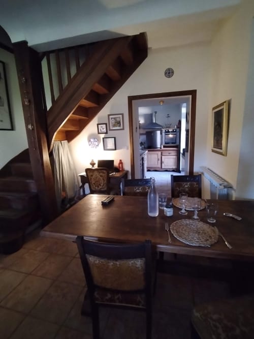 Dining area in French countryside cottage with wooden stairs, set table, and kitchen doorway visible