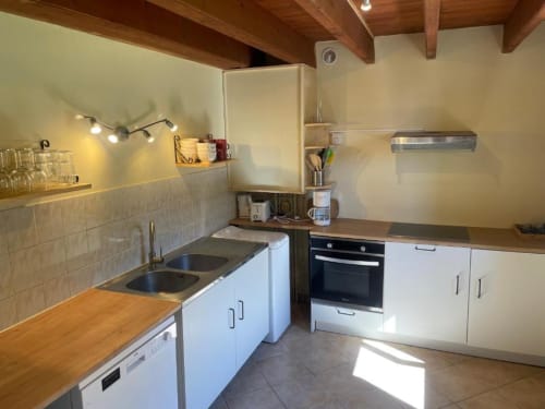 Cuisine moderne du gîte Château de Vaux Morvan avec cabineterie blanche, cuisinière inox, double évier et poutres apparentes