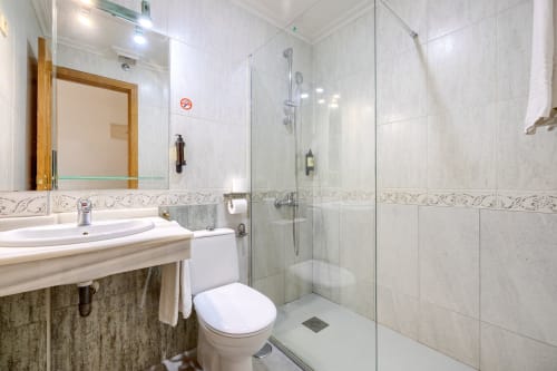 Baño moderno del Hostal El Molino con mampara de ducha cristal, lavabo blanco y paredes alicatadas en Collado Villalba